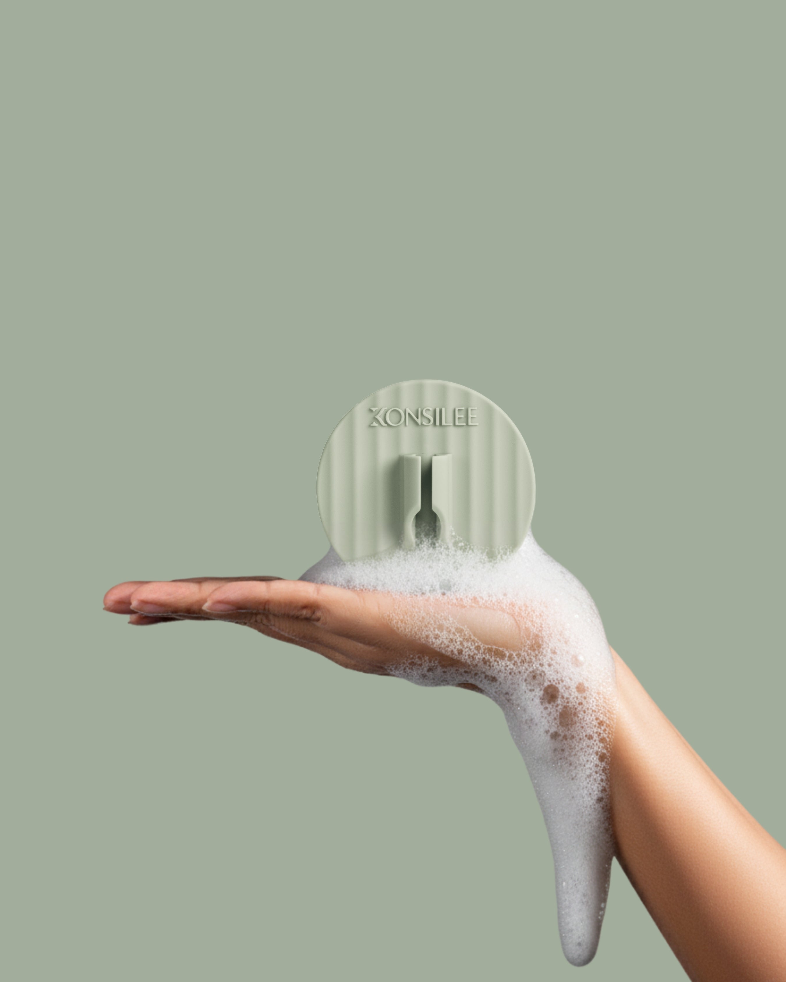A light-green, fluted silicone razor holder, held in a person’s soapy hand. The hook is a circle shape and has an embossed Konsilee logo. The background is a solid light-green shade.
